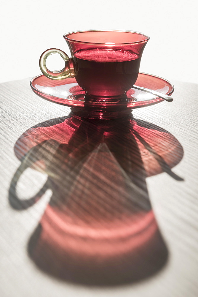 A Red Glass Cup A Saucer With A Beverage Reflected On A White Surface, Locarno, Ticino, Switzerland