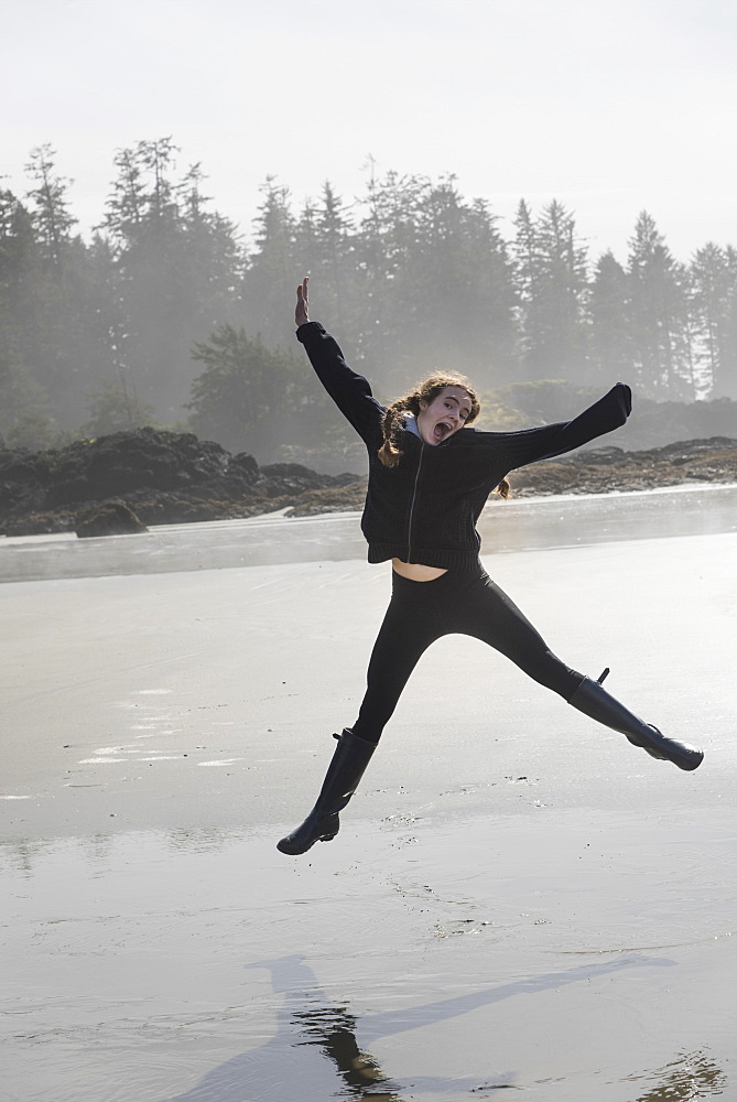 A Girl Leaping In Mid-Air On A Wet Beach, Tofino, British Columbia, Canada