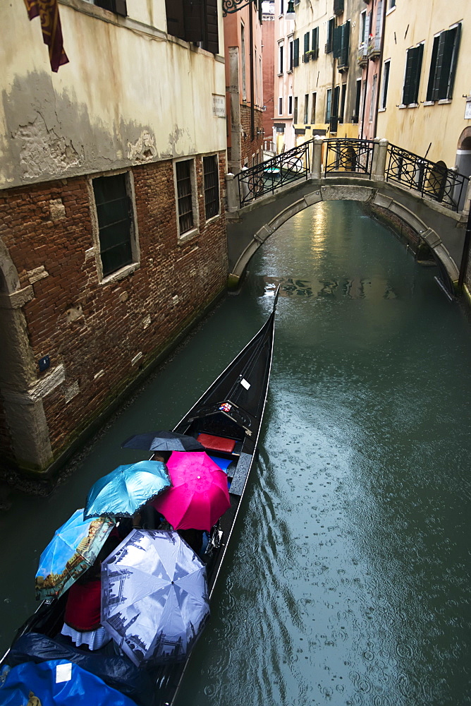 A Gondola Traveling Through A Canal On A Rainy Day With The Passengers Holding Umbrellas, Venice, Italy