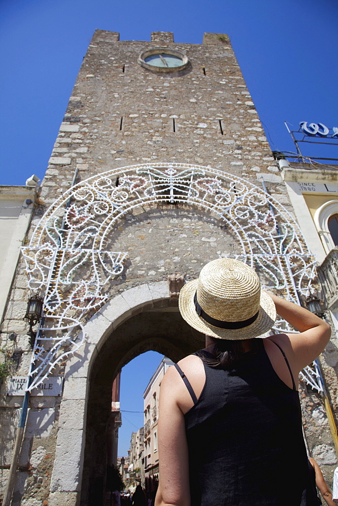 Female Tourist Looking At The Clock Tower Of San Giuseppe Church; Taormina, Sicily, Italy