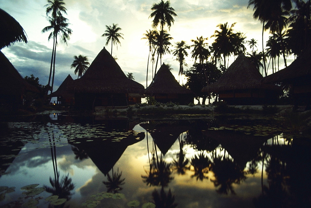 Reflection of huts and trees in water, Huahine Island, French Polynesia