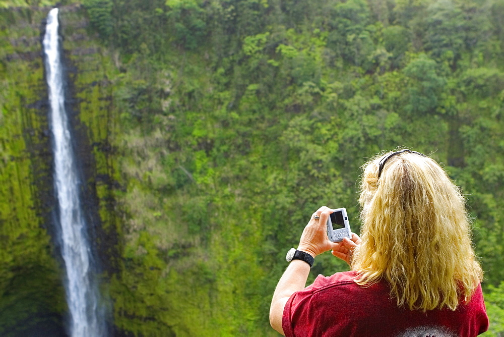 Rear view of a woman taking a photograph of a waterfall, Akaka Falls, Akaka Falls State Park, Hilo, Big Island, Hawaii Islands, USA