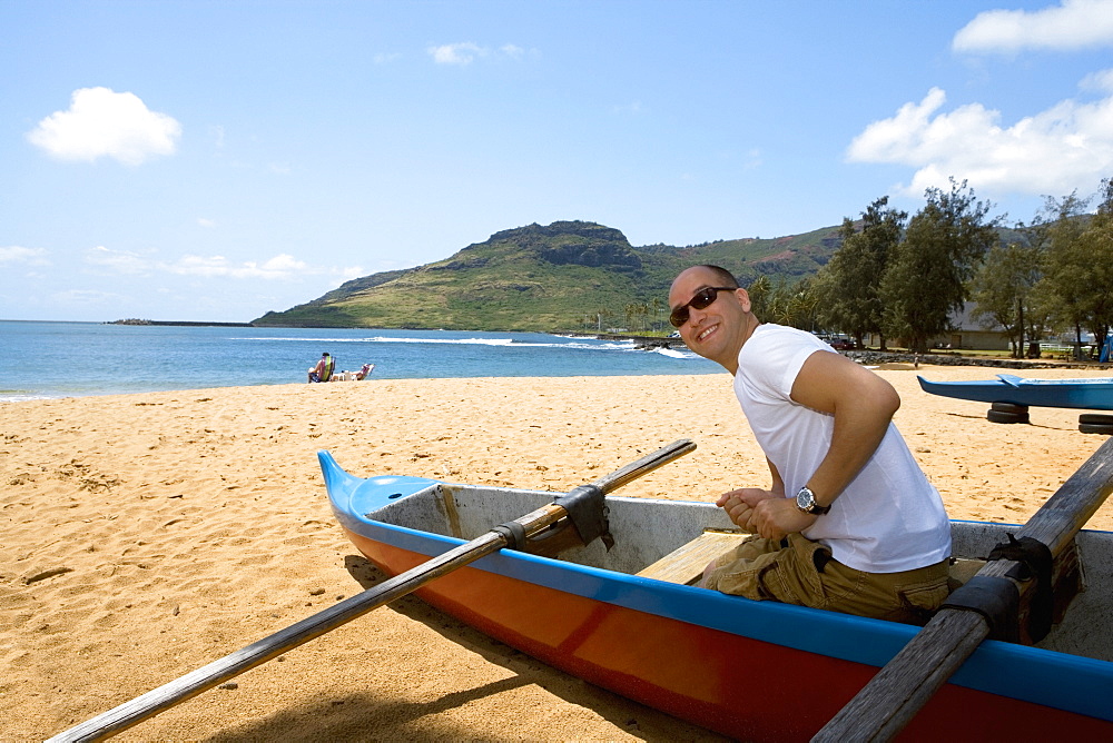 Side profile of a mid adult man sitting in a boat on the beach, Nawiliwili Beach Park, Kauai, Hawaii Islands, USA