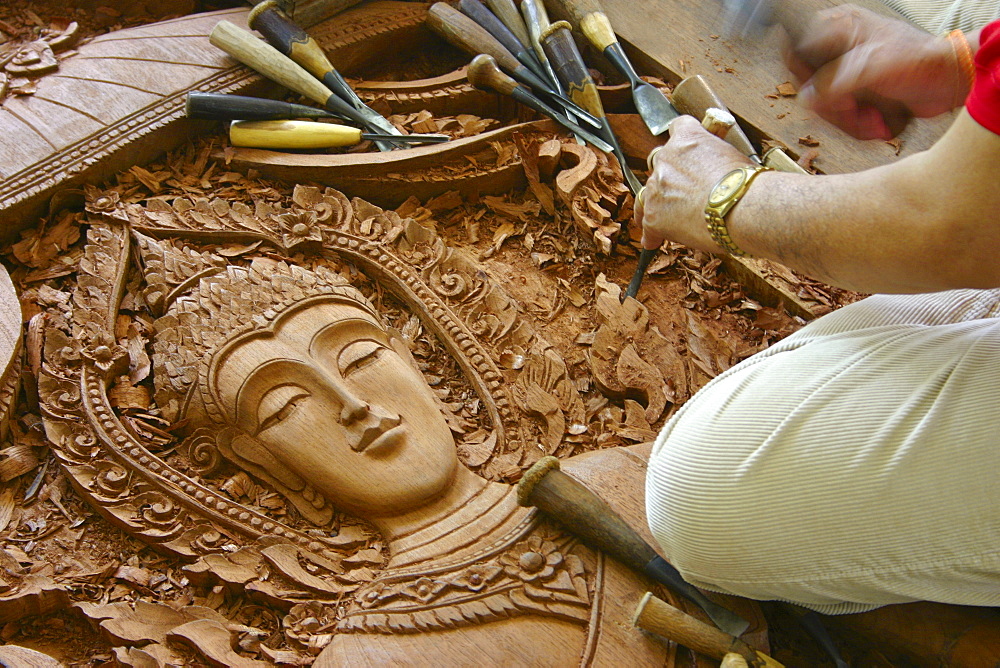 Close-up of a person's hands carving a statue of Buddha on wood, Chiang Rai, Thailand