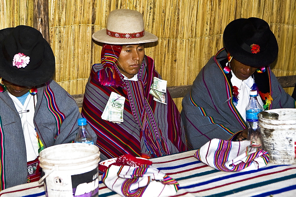 Two mature men sitting with a groom at a table, Taquile Island, Lake Titicaca, Puno, Peru