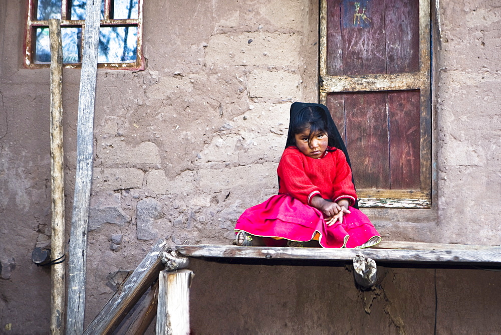 Portrait of a girl sitting in front of the gate of a house, Taquile Island, Lake Titicaca, Puno, Peru