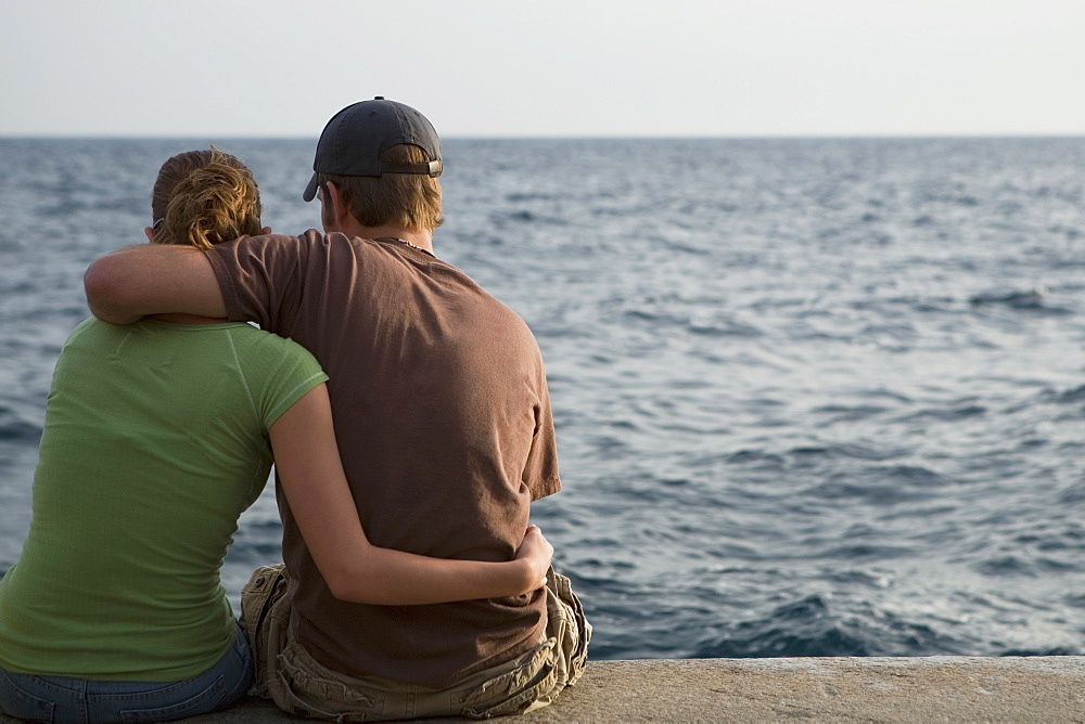 Rear view of a couple sitting at the seaside, Italian Riviera, Mar Ligure, Genoa, Liguria, Italy