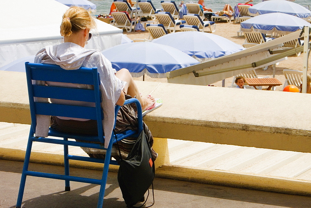 Rear view of a woman sitting in an armchair on the beach, Plage De La Croisette, Cote d'Azur, Cannes, Provence-Alpes-Cote D'Azur, France