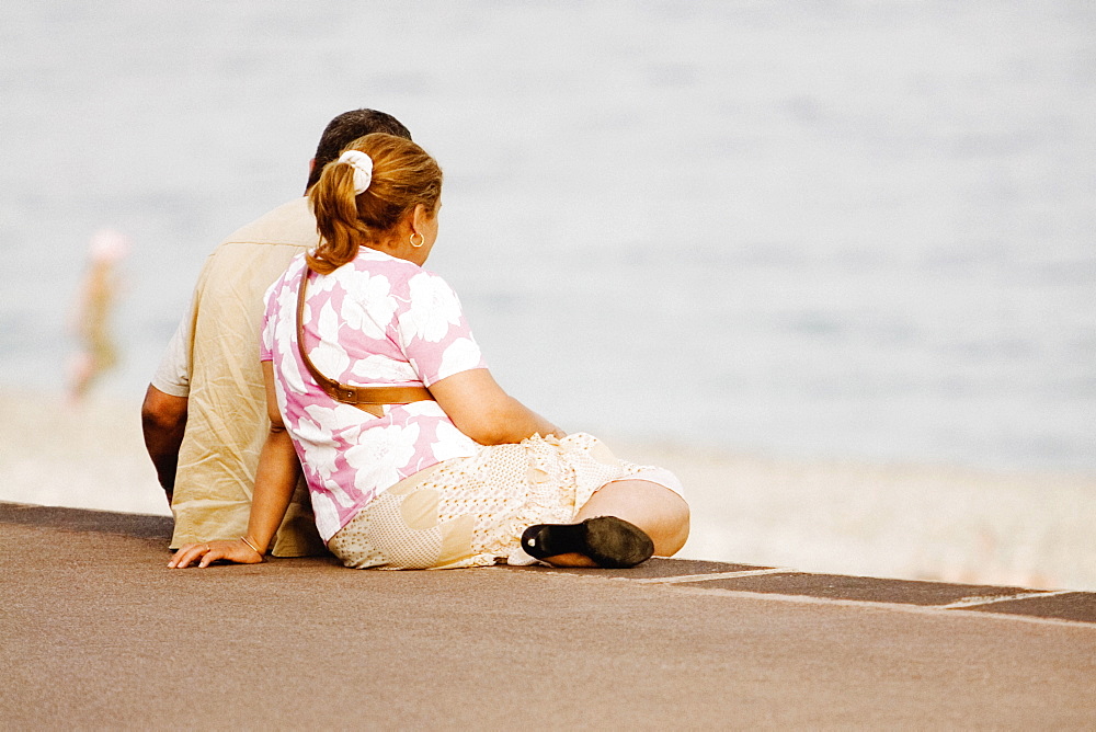 Couple sitting on the beach, Promenade Des Anglais, Nice, Provence-Alpes-Cote D'Azur, France