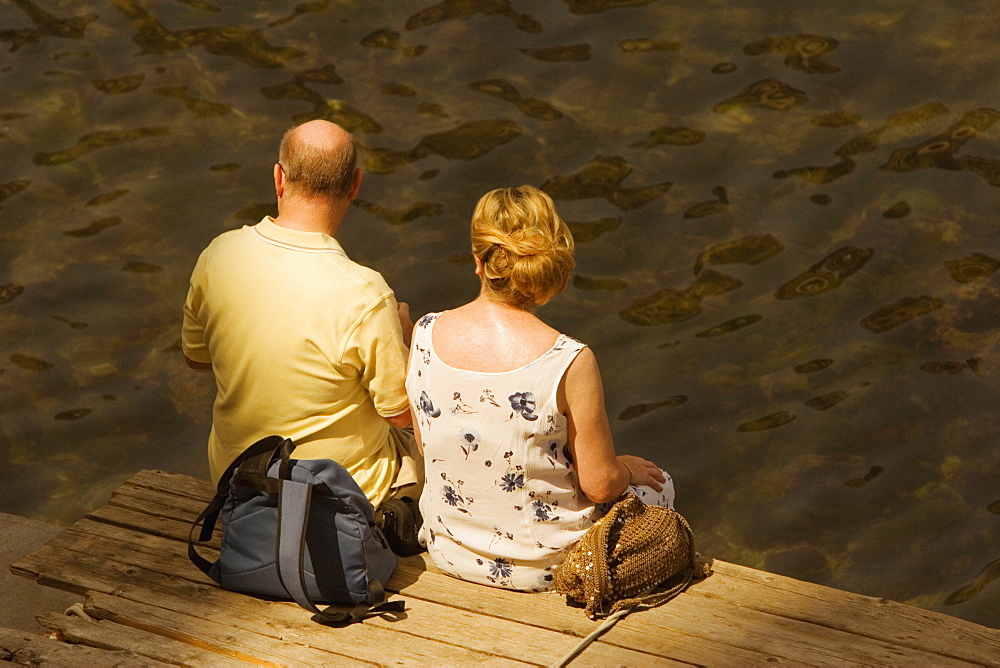 Rear view of a couple sitting on a boardwalk, Bay of Naples, Sorrento, Sorrentine Peninsula, Naples Province, Campania, Italy