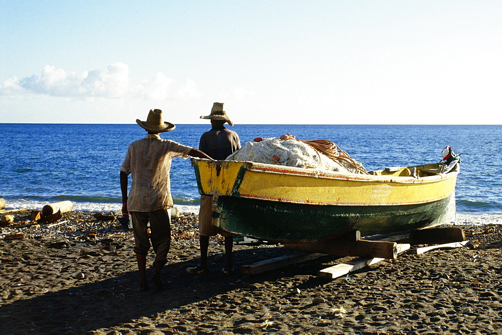 Rear view of two men near a boat on a beach on the island of Martinique, Caribbean