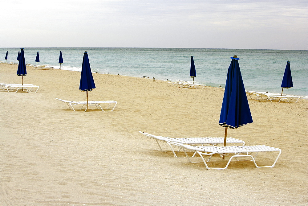 Empty lounge chair and a folded beach umbrella on the beach