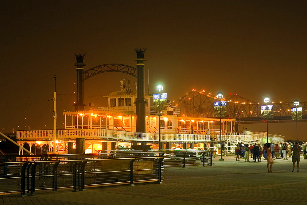 Group of people walking in front of an illuminated paddle steamer moored at a harbor, New Orleans, Louisiana, USA