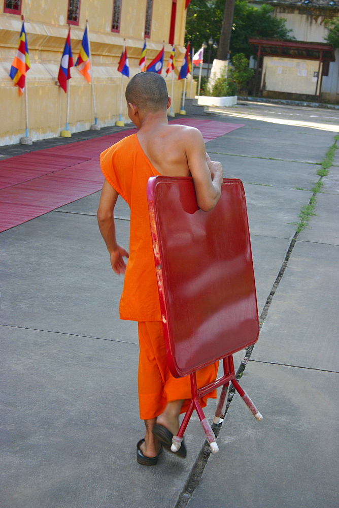 Rear view of a monk carrying a folded table and walking on the road, Vientiane, Laos