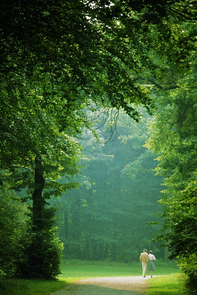 Rear view of two people walking in a park, Munich, Germany