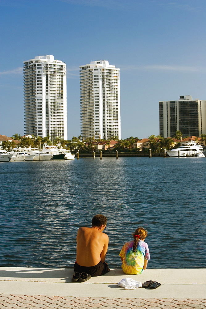 Rear view of a man and his daughter sitting on the edge of a pier