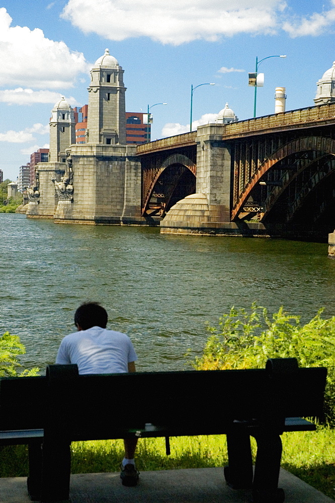 Rear view of a man sitting on a bench near a bridge, Longfellow Bridge, Charles River, Boston, Massachusetts, USA