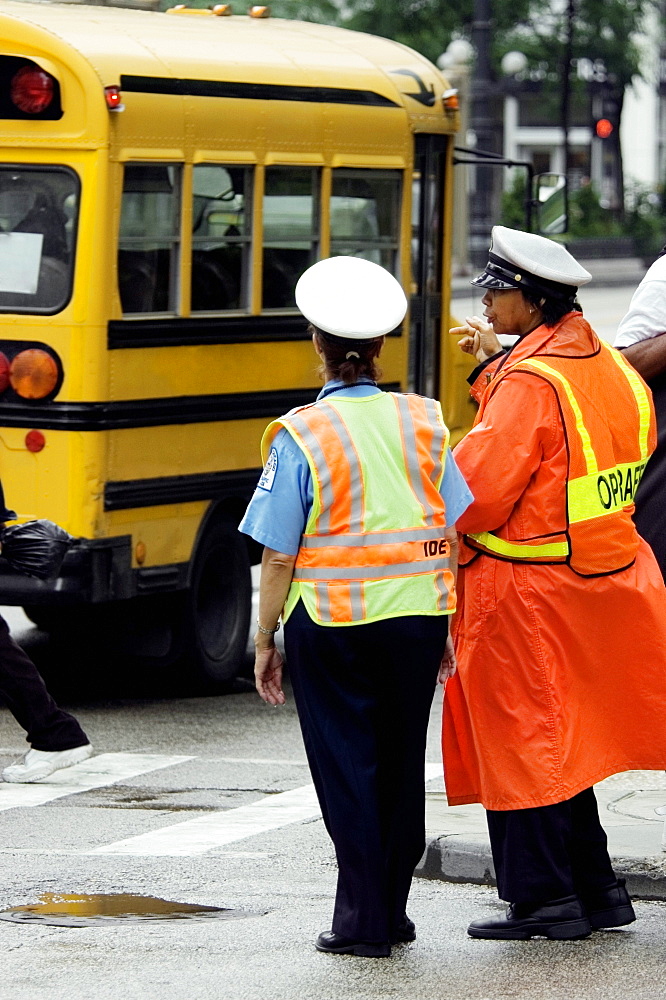 Rear view of two crossing guards standing beside a school bus, Chicago, Illinois, USA