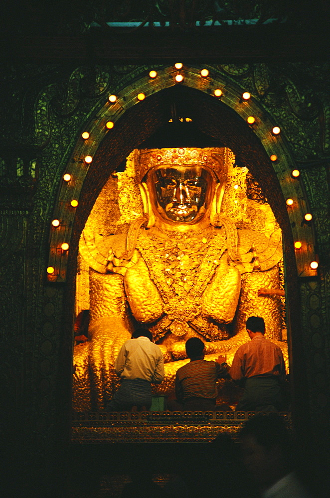 Rear view of three men praying in front of a statue of Buddha, Mandalay, Myanmar