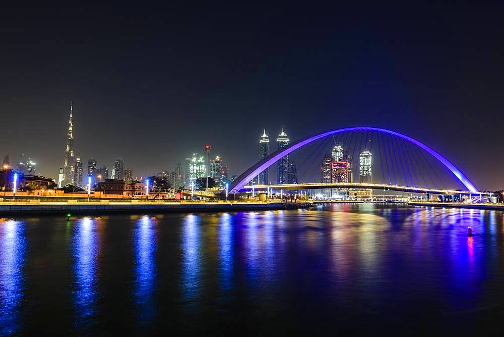 Night, cityscape of Dubai, tall buildings and waterfront, and arch over the creek.