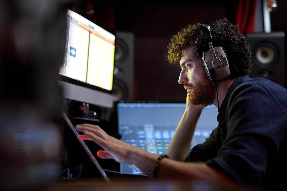 Man working in music studio using computer wearing head phones