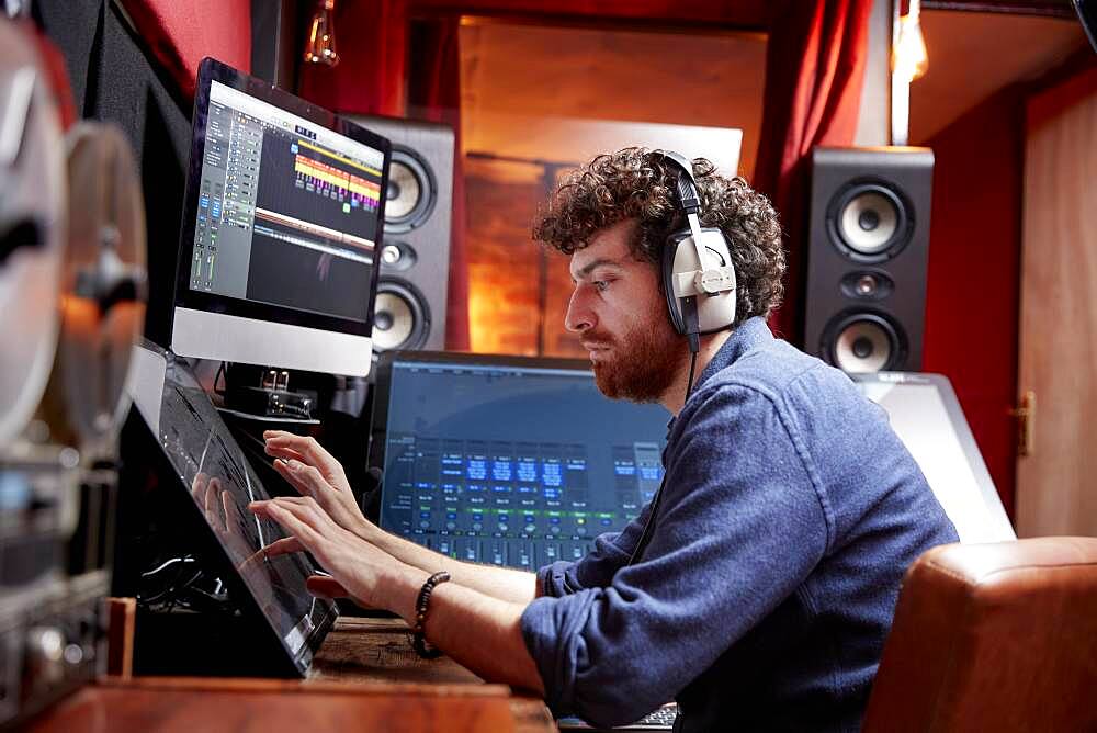 Man working in music studio using computer wearing head phones