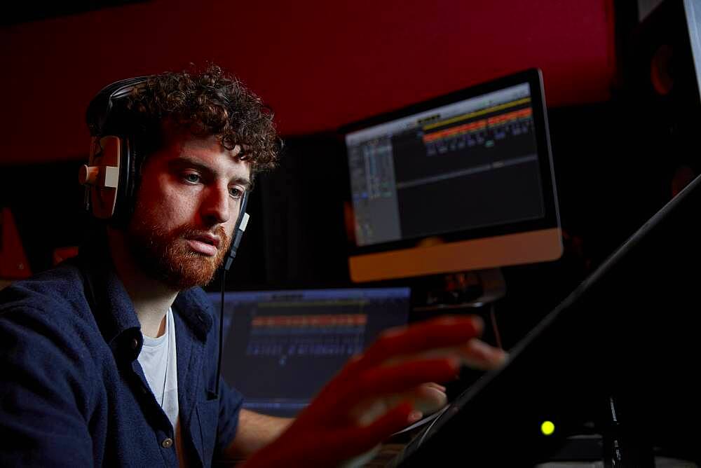 Man working in music studio using computer wearing head phones