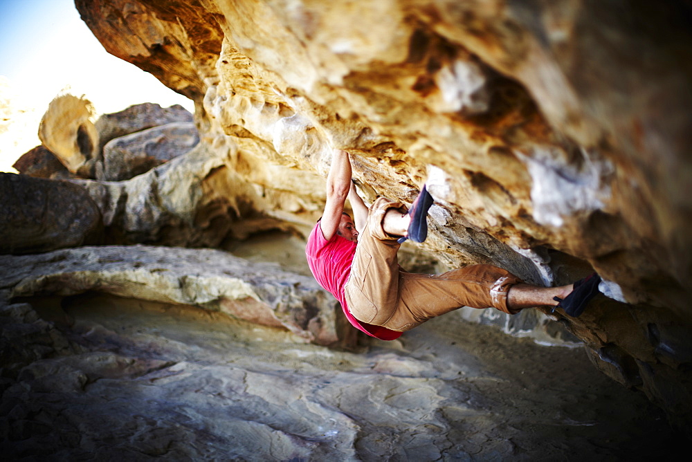 A man free climbing on the overhang of a rock face, with minimum equipment, USA