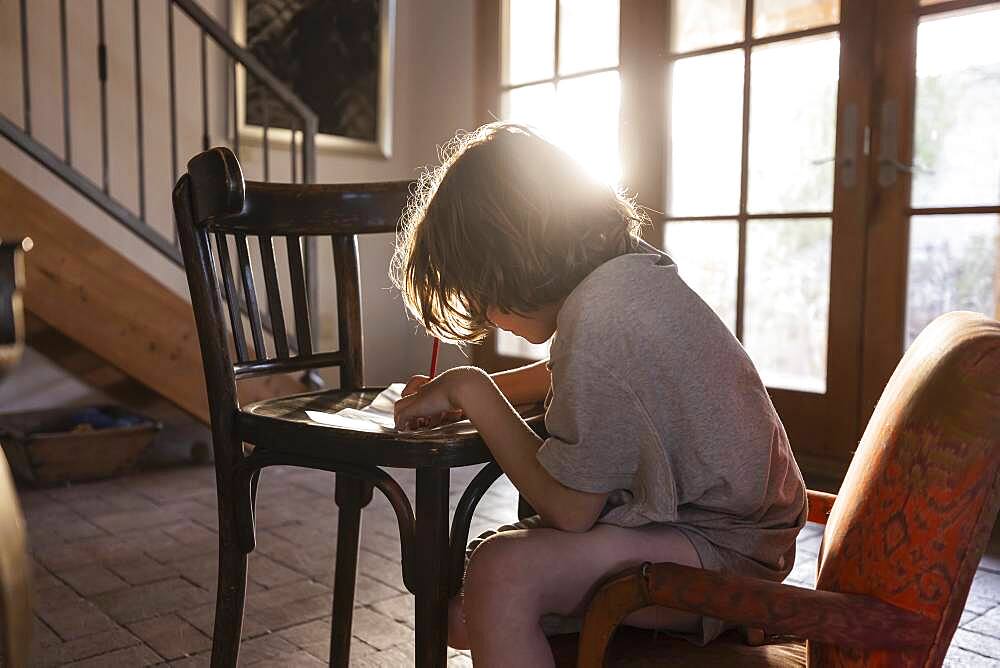 young boy writing on small chair at sunset