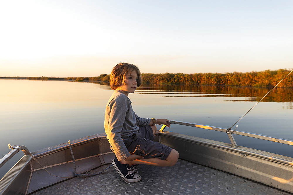 Young boy on a boat on the waters of the Okavango Delta at sunset, Botswana.