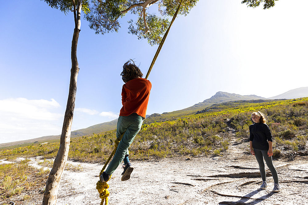 Teenage girl and younger brother using rope swing on a hiking trail