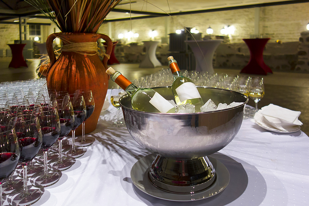 Wine bottles in metal ice bucket. Cooler with ice cubes. Wine glasses.