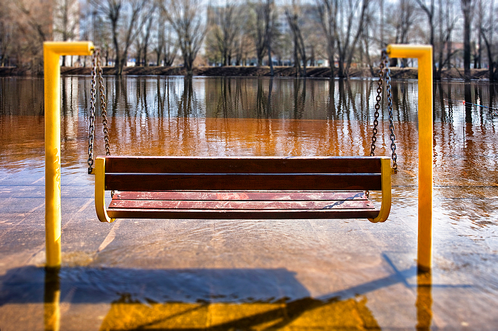 Empty hanging bench swing surrounded by hard frozen ice, riverbank