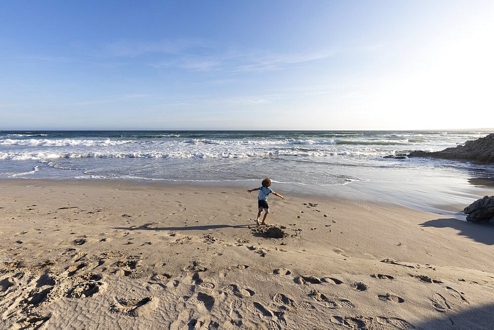 Young boy running in open space on a beach on the Atlantic coast, Grotto Beach, Western Cape, South Africa