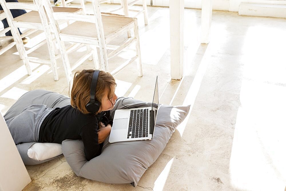 Eight year old boy lying on the floor on cushions using a laptop, Stanford, South Africa