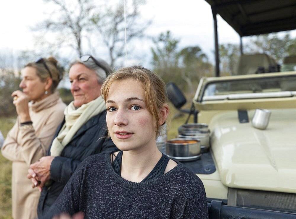 Three generations of women, a grandmother, mother and teenage girl by a safari jeep, Okavango Delta, Botswana