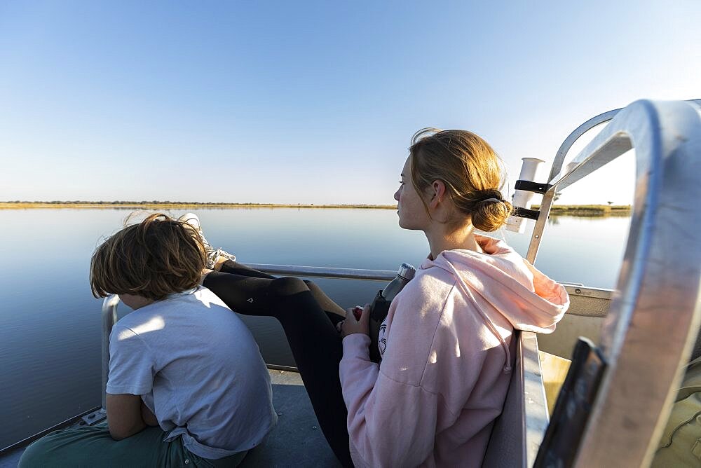 Two children on a boat, a boy and his teenage sister looking out over the water, Okavango Delta, Botswana