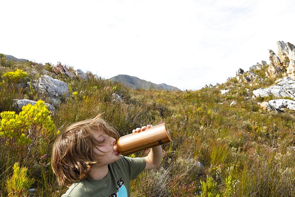 Young boy on nature trail, stopping to drink from a water bottle, Phillipskop Nature Reserve, Western Cape, South Africa