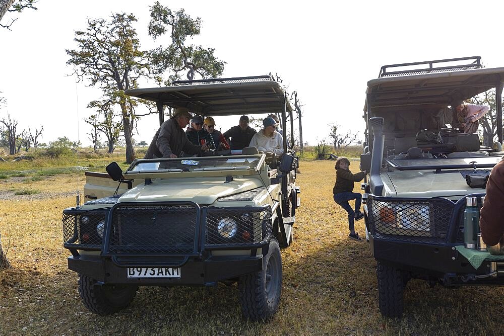 Two safari vehicles side by side, a boy climbing from one to another, Okavango Delta, Botswana