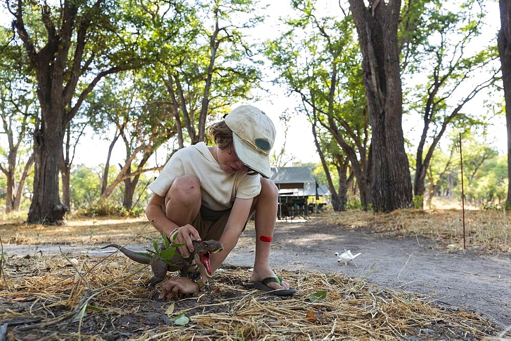 Young boy in tented safari camp paying with a green dinosaur toy, Okavango Delta, Botswana