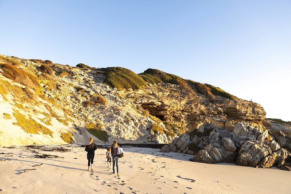 A family walking along a sandy beach towards the cliffs, Walker Bay Nature Reserve, South Africa