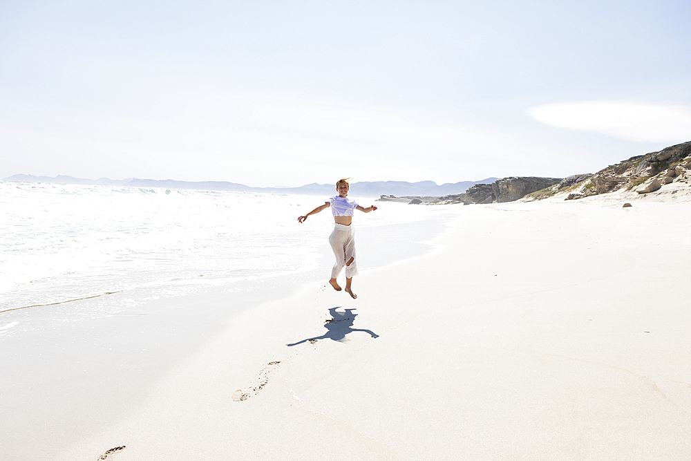 Teenage girl dancing alone on a sandy beach in South Africa by the water's edge