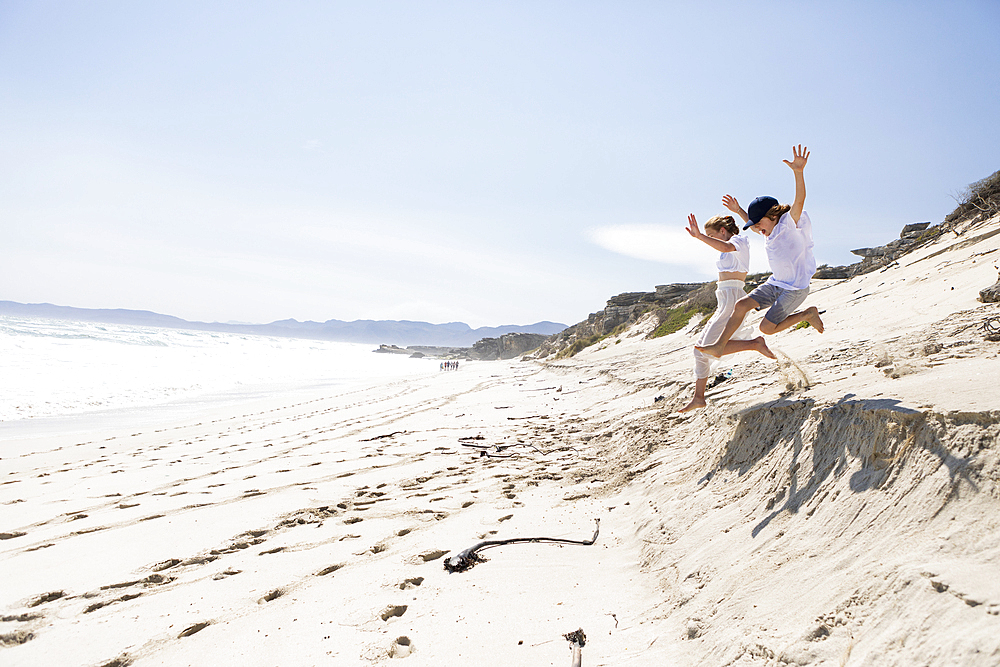 Two children leaping off sand dune on a beach