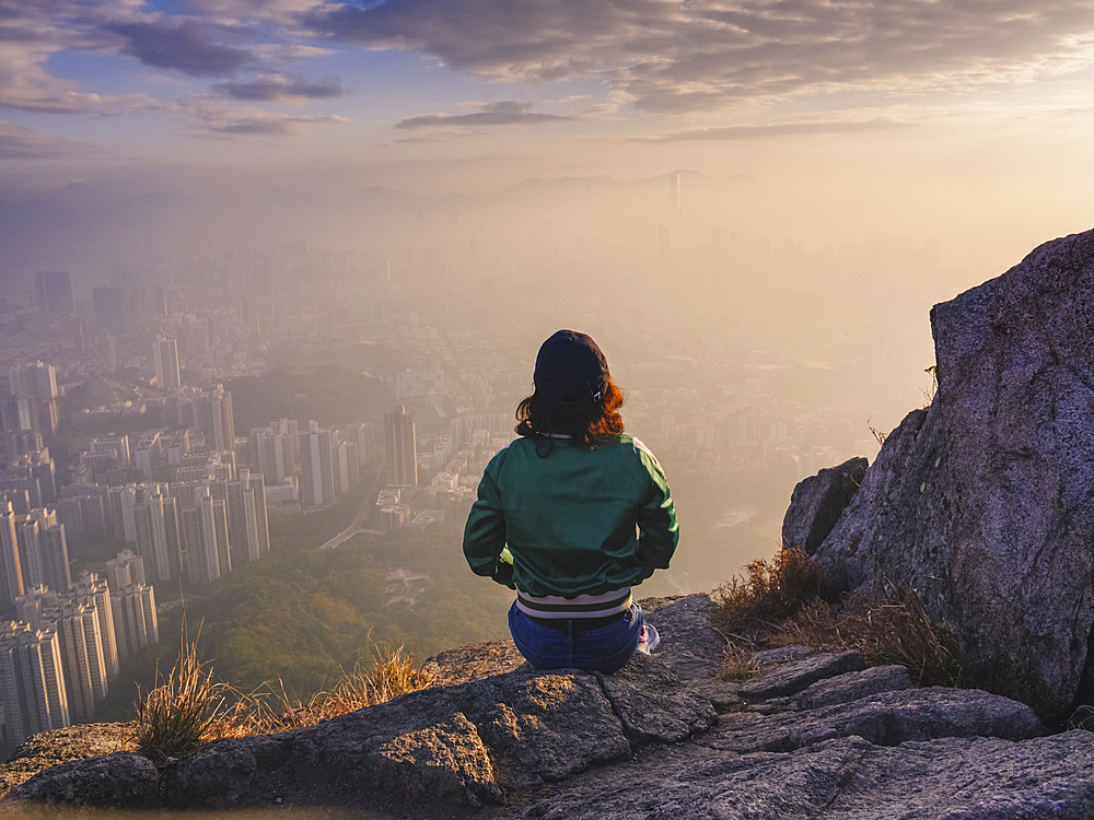 Woman sitting on rock in hills above Hong Kong looking down over the city.