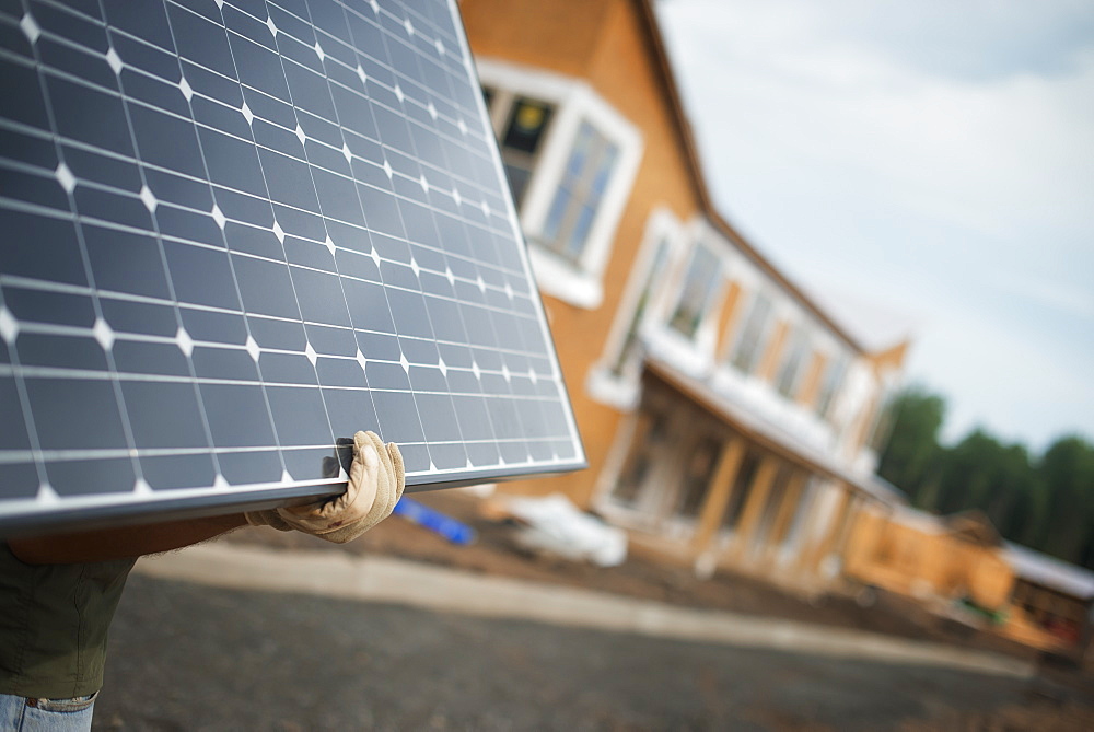 A workman carrying a large solar panel at a green house construction site, Woodstock, New York, USA