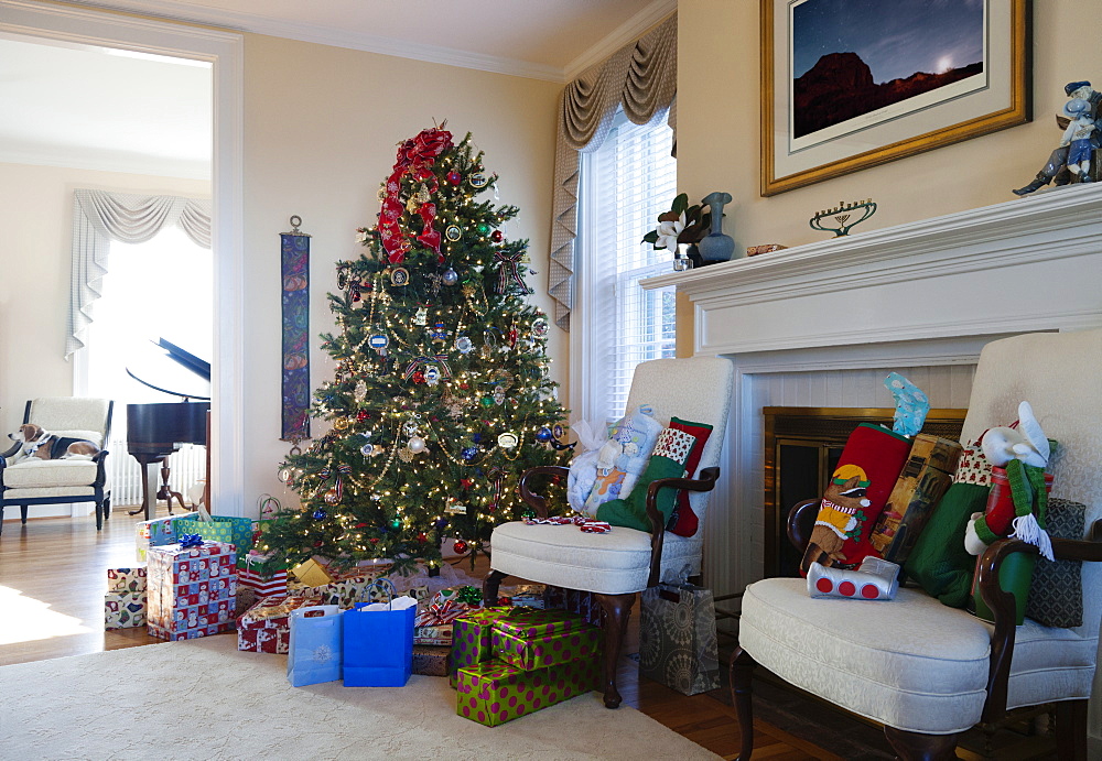 Living room with Christmas tree and gifts, traditional decorations, fireplace and furniture.