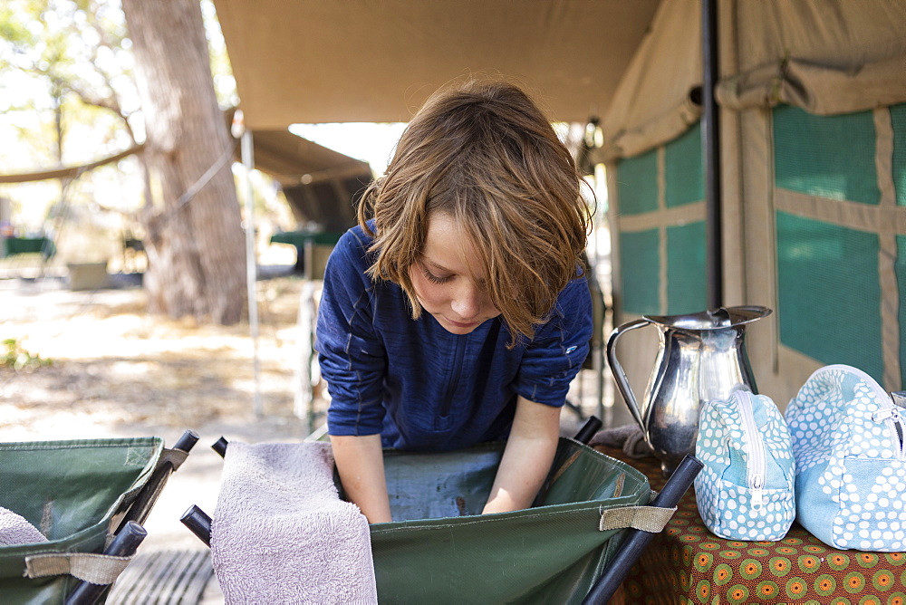 A boy washing his face in a basin at a campsite in the Okavango, Okavango Delta, Botswana