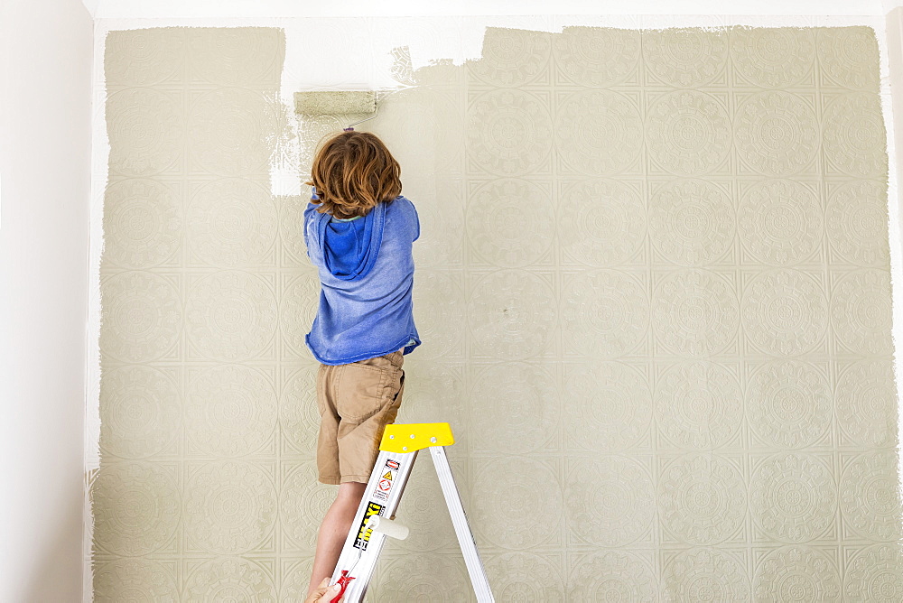 A boy using a paint roller to paint wall