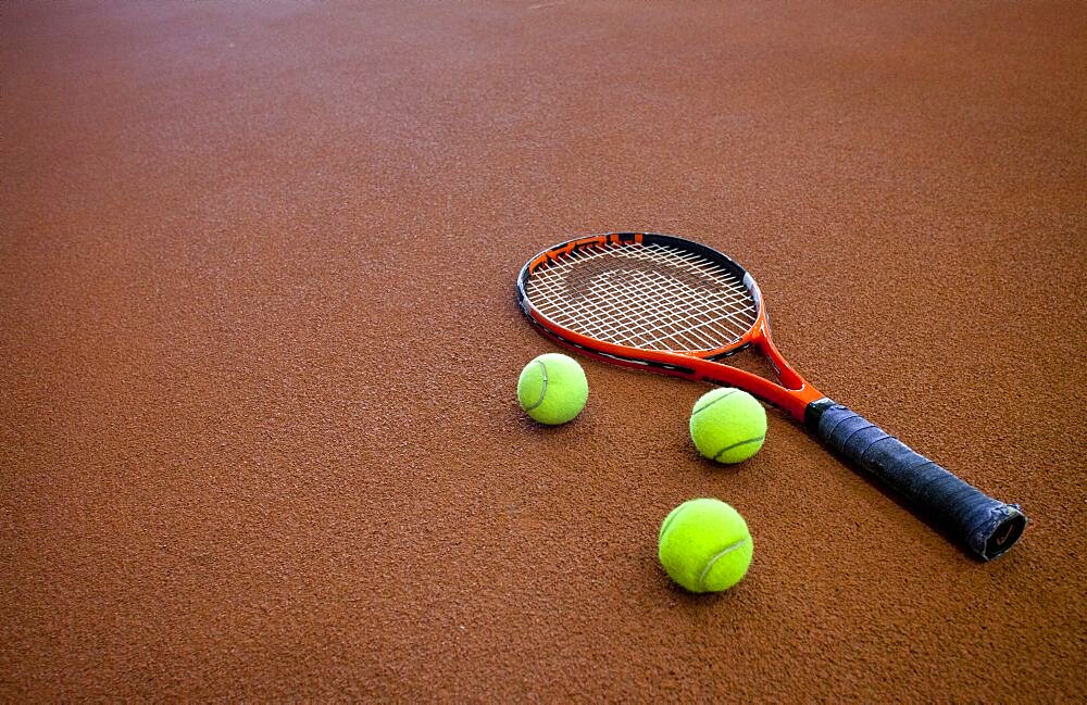 A hard tennis court and a tennis raquet,with three balls.