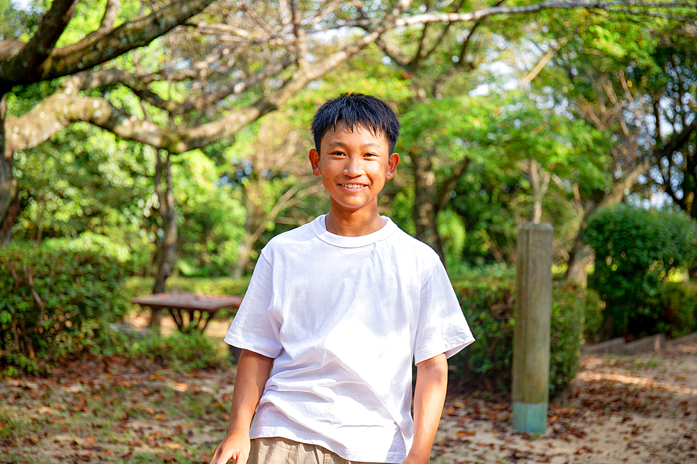 A 13 year old boy in a white teeshirt, smiling, outdoors in a park.